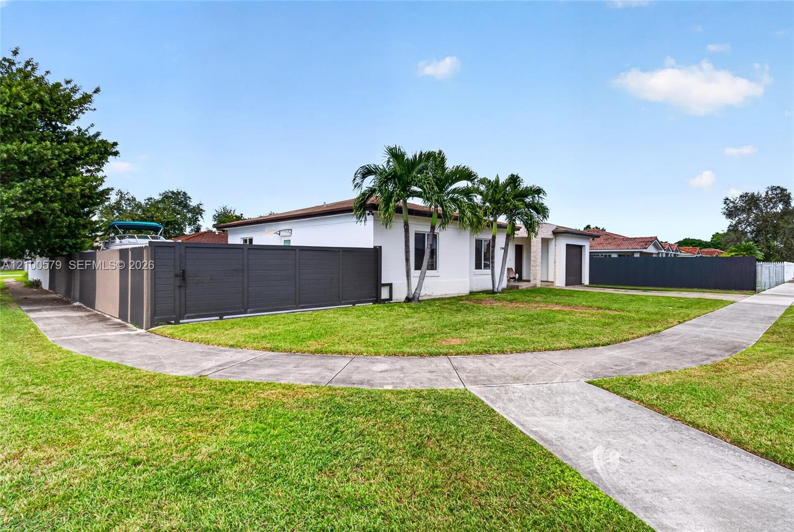 Single-story residence featuring a smooth stucco exterior, attached garage, solid-panel privacy fencing, and mature palm trees