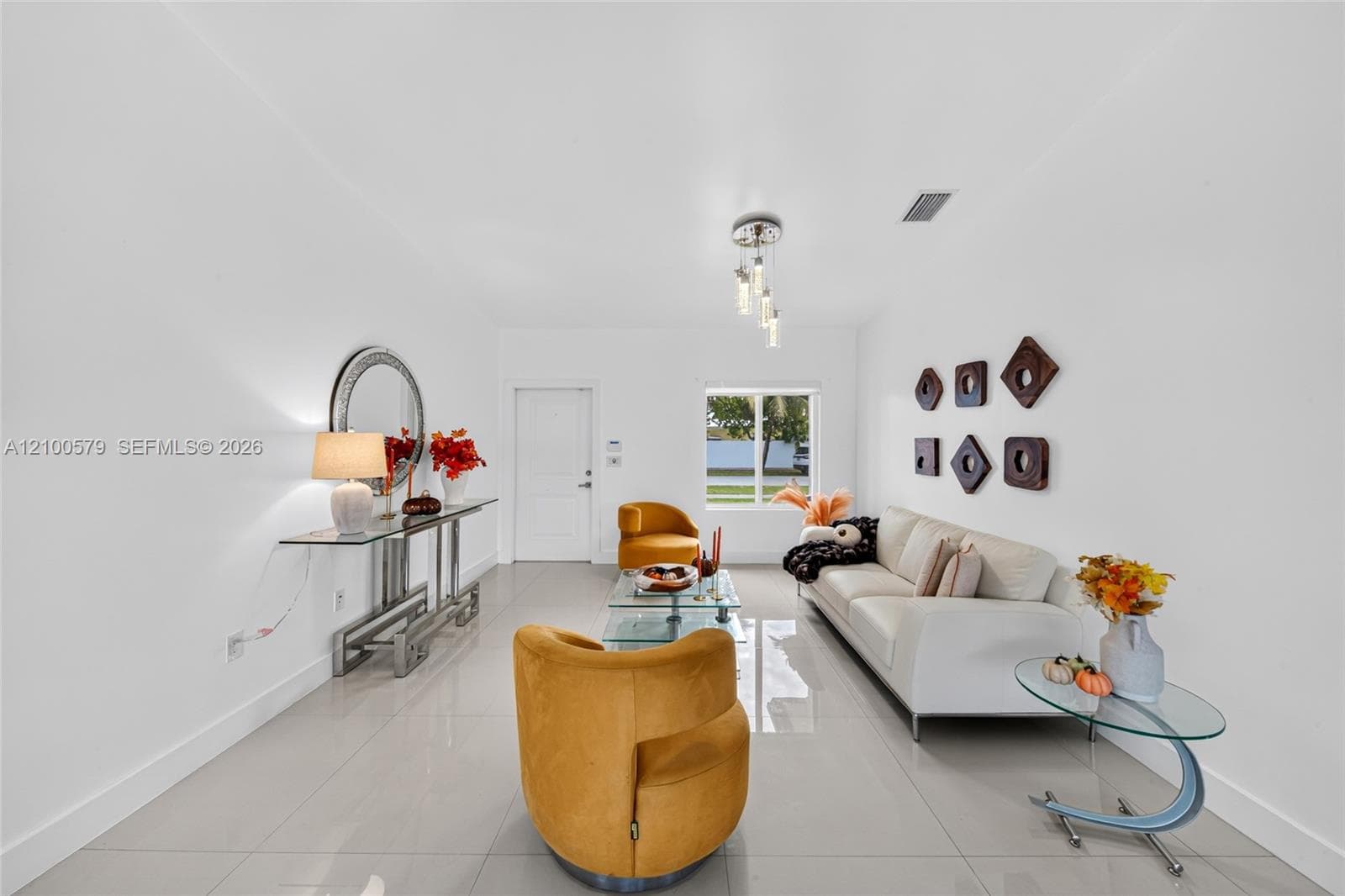 Open-concept living space featuring high-gloss tile flooring, multi-light pendant fixture, and natural light via window and exterior door