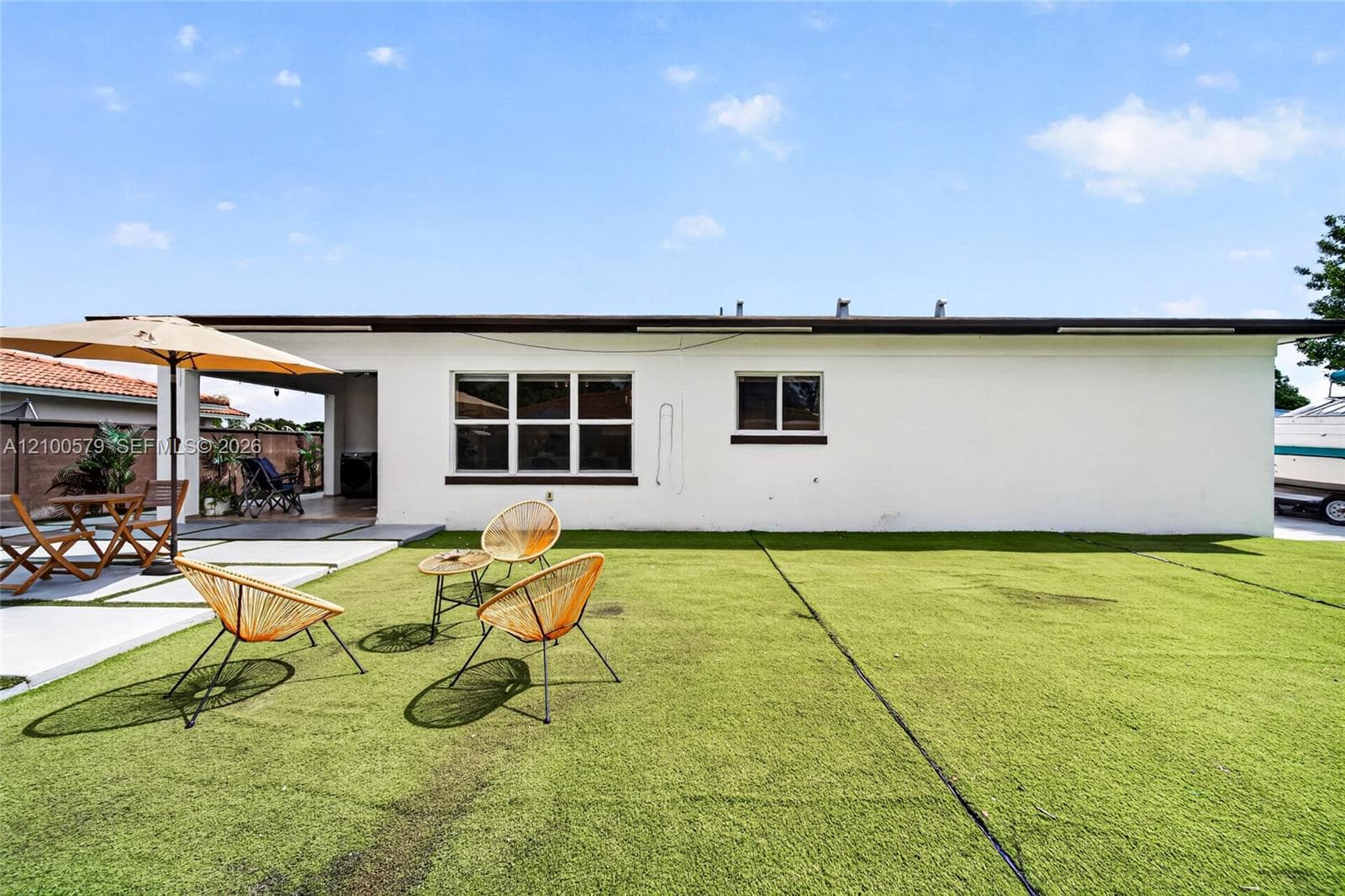 Backyard featuring a covered patio, concrete hardscaping, and synthetic turf lawn