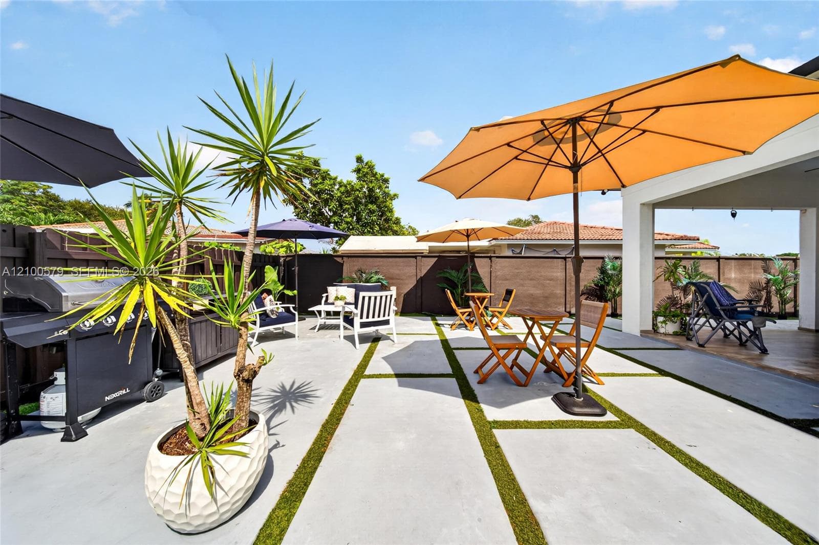 Rear patio featuring large-format concrete pavers with artificial turf inlay, covered porch area, and dark-finished privacy fencing