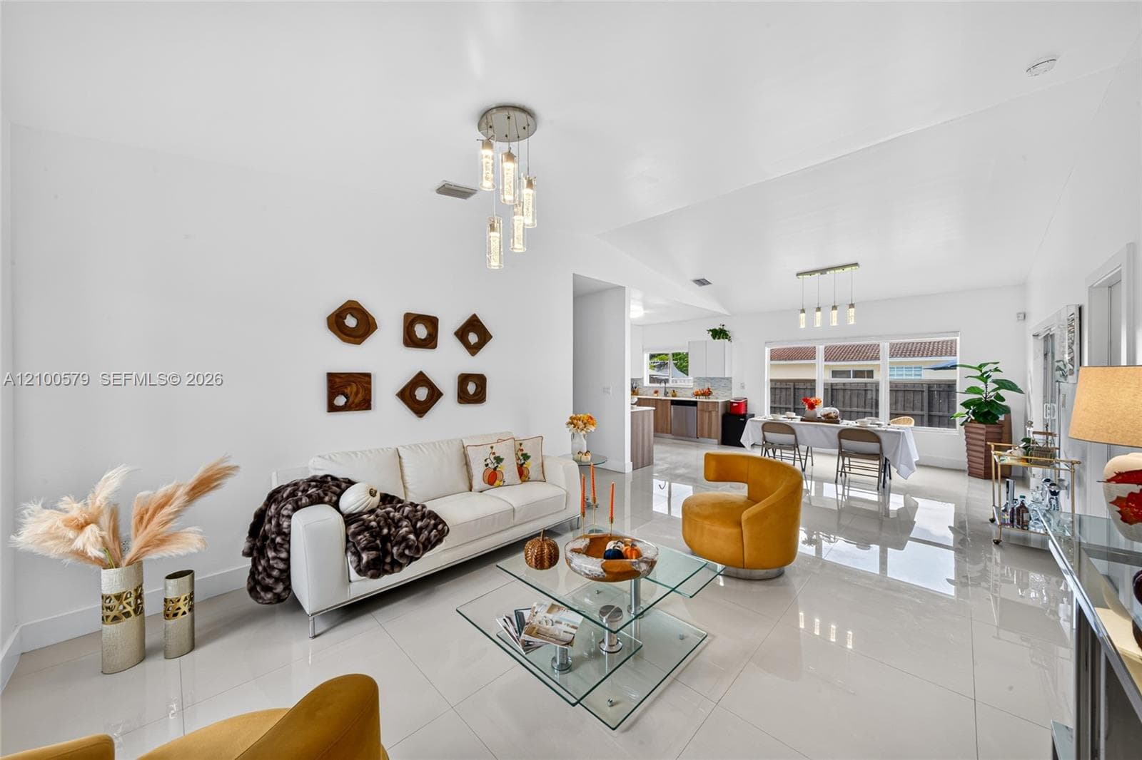 Open-concept interior featuring large-format tile flooring, vaulted ceilings, multi-pendant lighting fixtures, and expansive windows