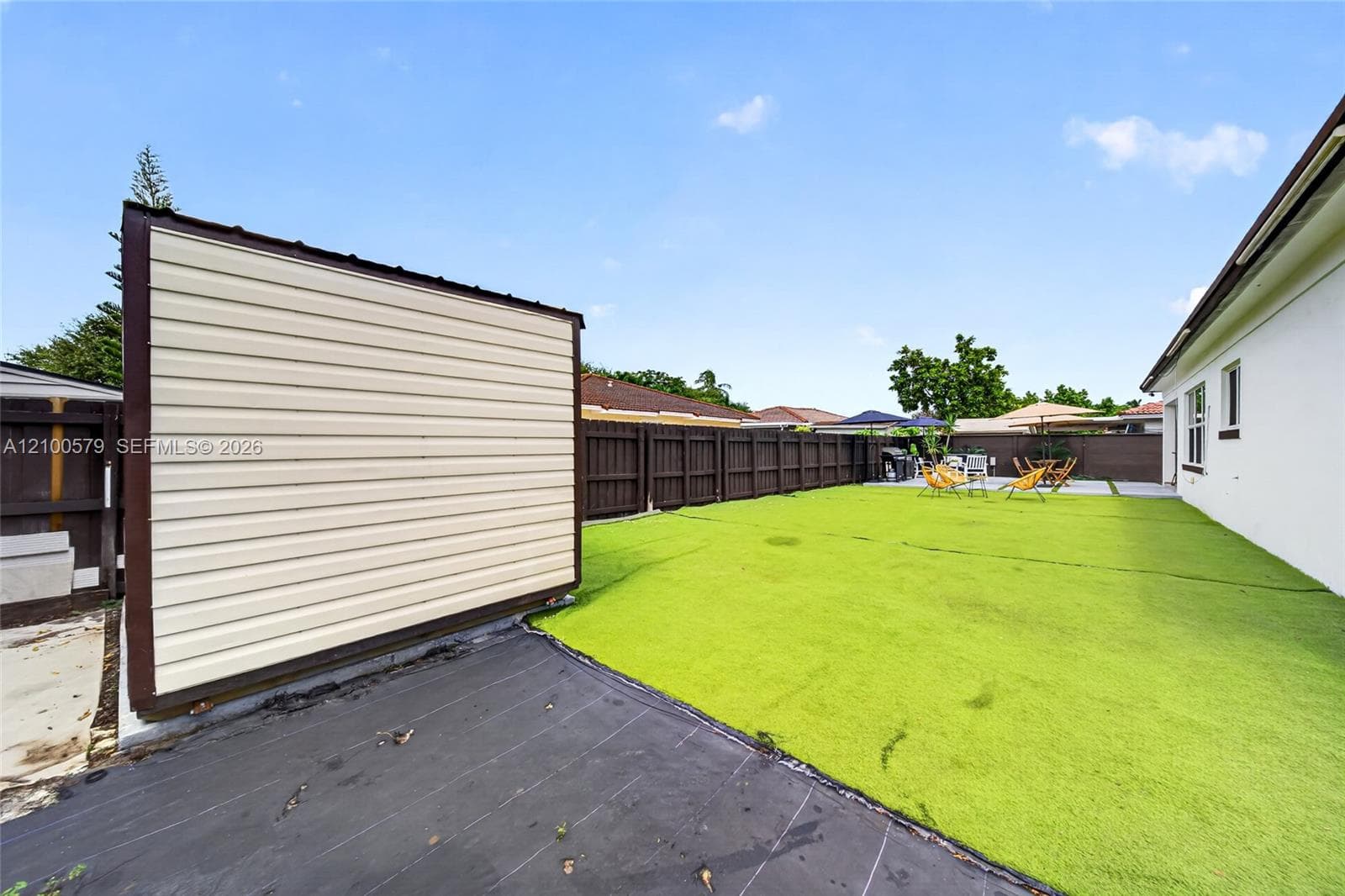 Fenced backyard featuring synthetic turf, a standalone storage structure with horizontal siding, and a paved concrete patio area