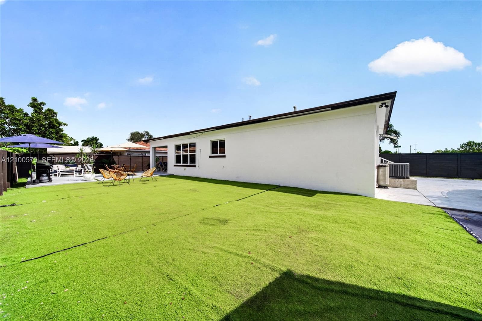 Spacious backyard featuring artificial turf, a paved concrete patio, and opaque privacy fencing