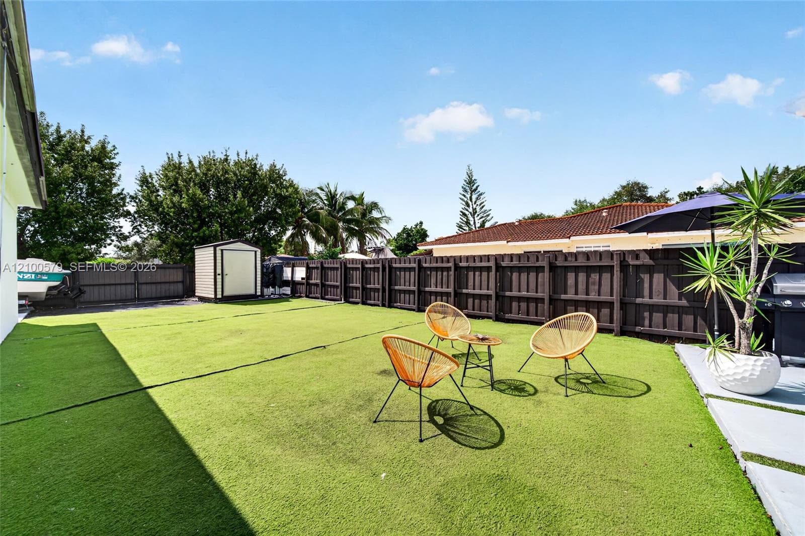 Expansive backyard featuring synthetic turf, full-height privacy fencing, concrete patio pavers, and a detached storage structure