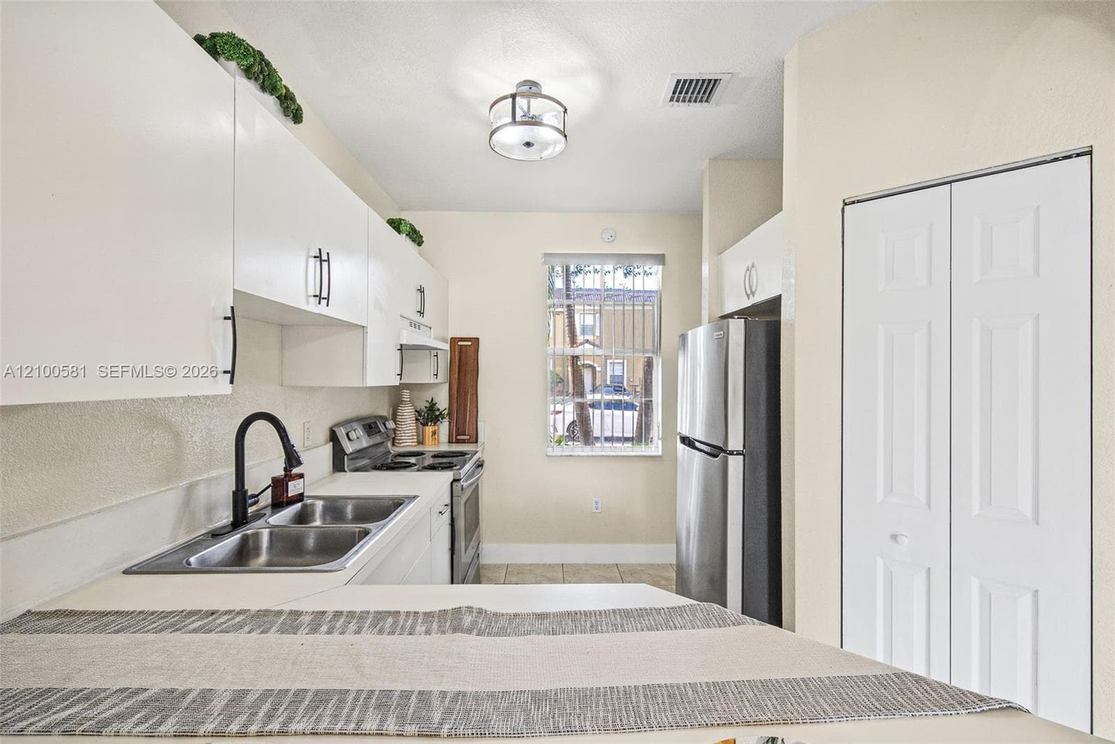 White cabinetry with matte black hardware, stainless steel electric range, dual-basin stainless steel sink with a matte black faucet, and tile flooring