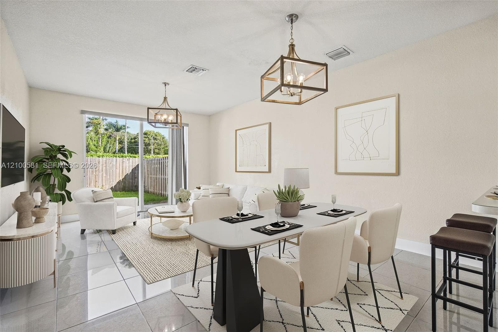 Open-concept living space featuring large-format tile flooring, dual geometric metal-frame pendant lighting, and sliding glass doors with access to an exterior fenced yard