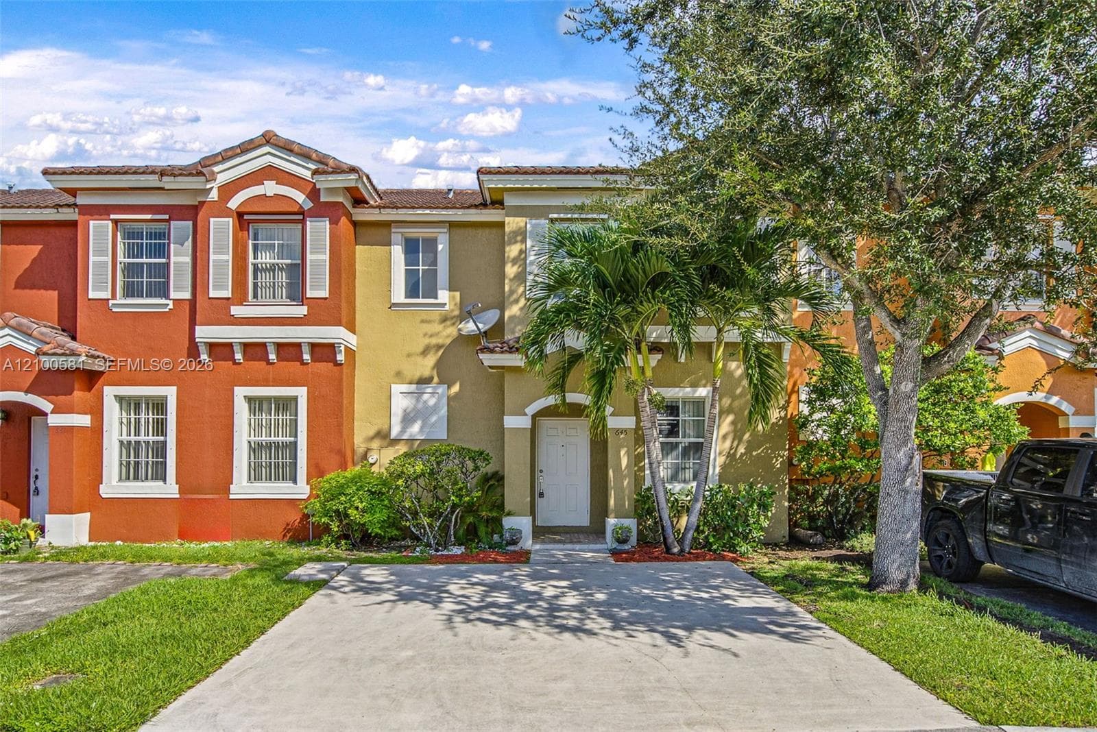 Two-story townhouse exterior featuring a concrete driveway, terracotta-style roof tiles, arched architectural details, and white-framed multi-pane windows