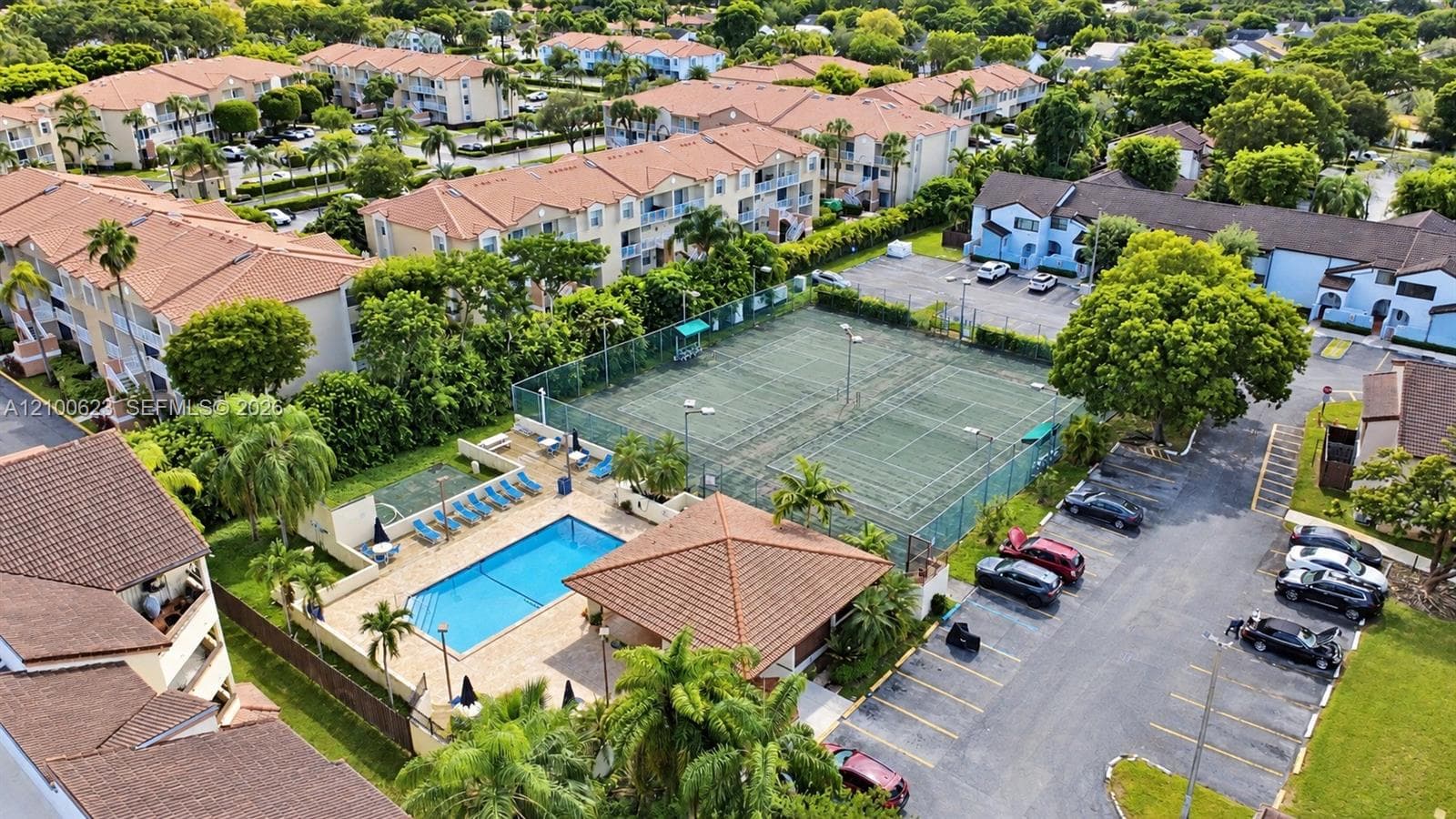 Aerial perspective featuring a swimming pool, fenced tennis courts, tile-roofed clubhouse and parking