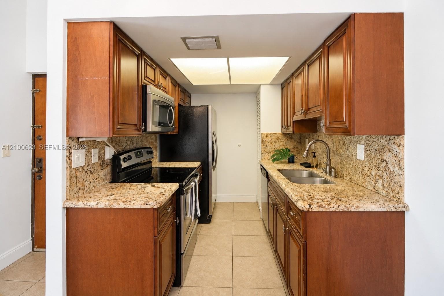 Kitchen featuring wood cabinetry, granite countertops, tile flooring, and integrated stainless steel appliances