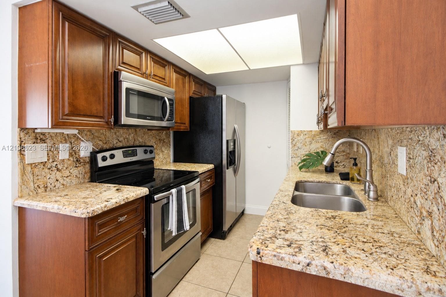 Kitchen featuring wood cabinetry, granite countertops and backsplash, stainless steel appliances, and dual-basin stainless steel sink with pull-down faucet