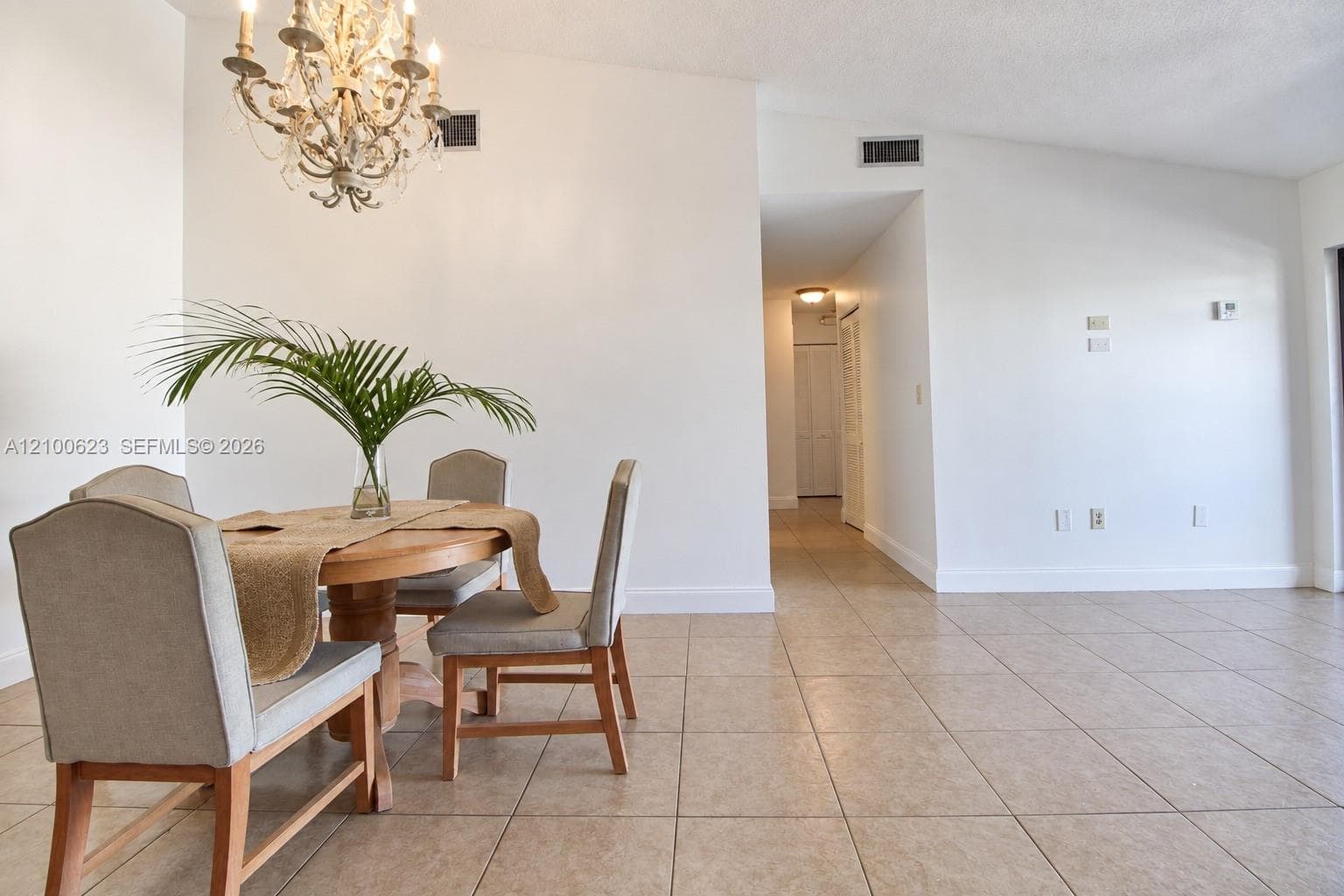 Open living area featuring vaulted ceilings, neutral ceramic tile flooring, and an ornate, multi-arm chandelier