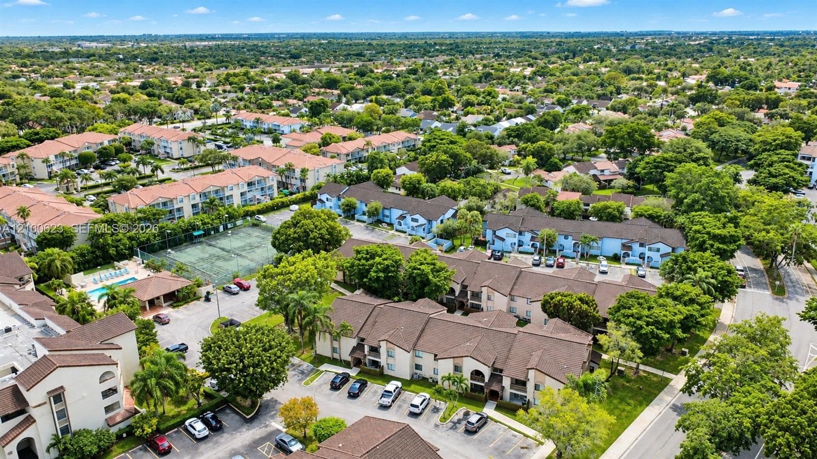 Aerial perspective of a multi-unit residential community featuring brown tile roofs, paved parking, a tennis court, and a swimming pool area