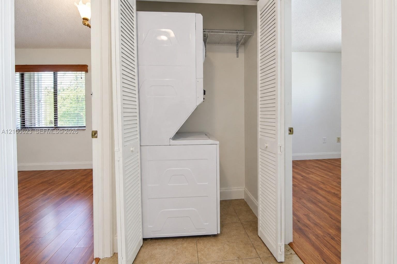 Laundry closet featuring a white stacked laundry unit, bi-fold louvered doors, wire shelving, and tile flooring