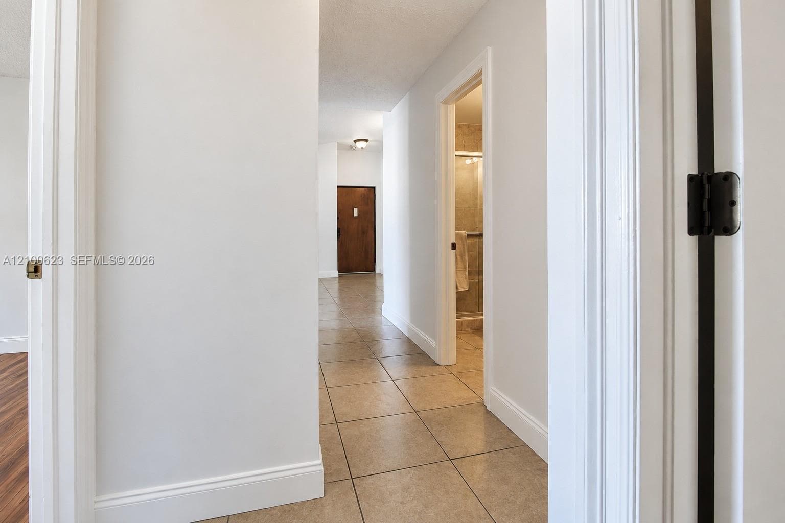 Hallway featuring neutral-toned tile flooring, solid wood-finish doors, and white-painted interior trim