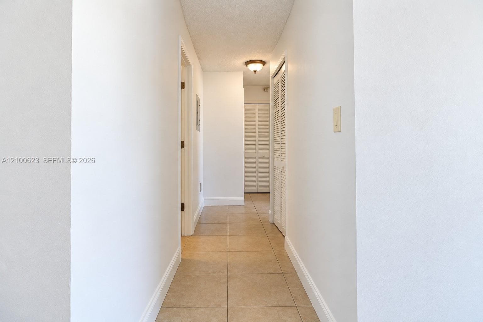 Hallway featuring neutral-toned tile flooring, white walls, and bi-fold closet doors