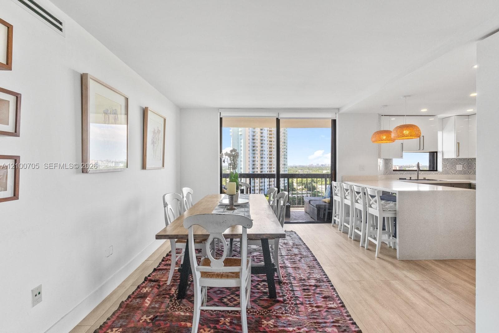 Open-concept kitchen featuring a quartz-topped island with seating, minimalist white cabinetry, wood-finish flooring, and floor-to-ceiling sliding glass doors