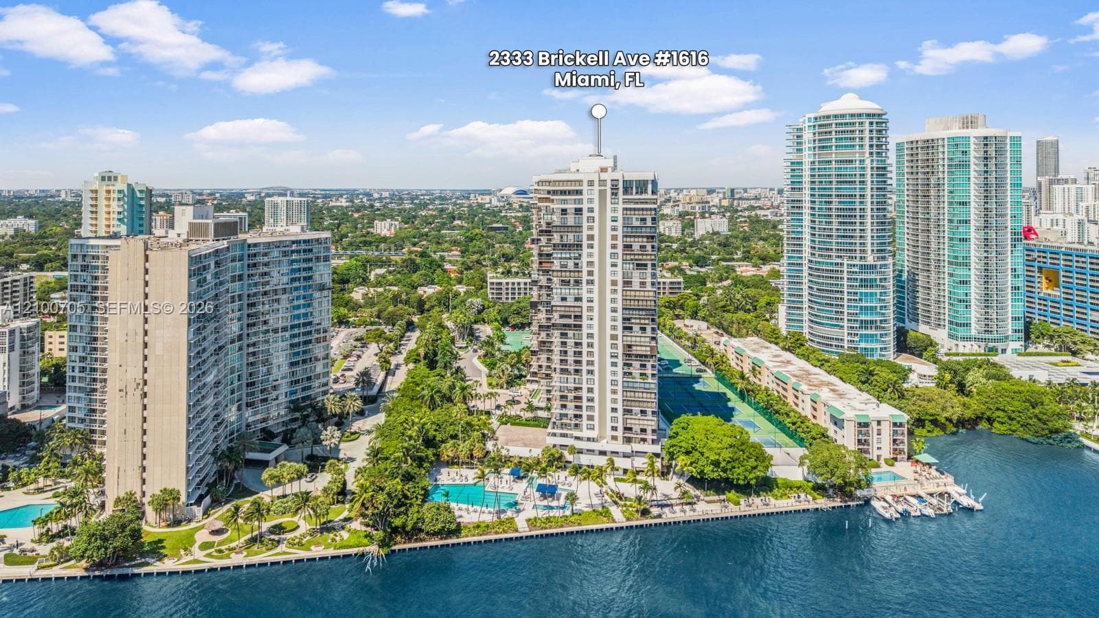 High-rise residential tower featuring a waterfront location, an outdoor swimming pool, paved walkways, mature landscaping, and a dock area