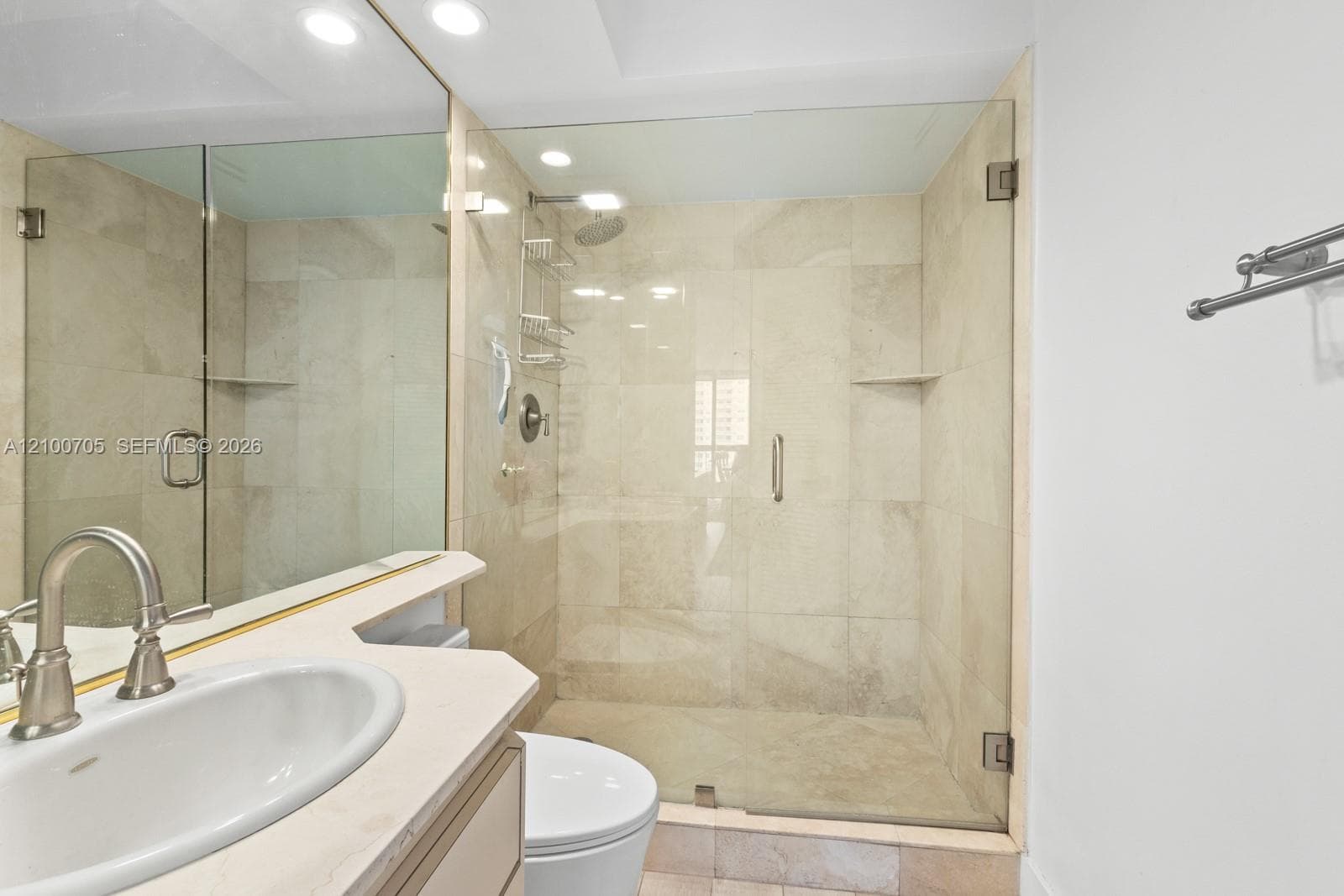 Walk-in shower with floor-to-ceiling neutral tile, glass enclosure, recessed lighting, and vanity with stone countertop