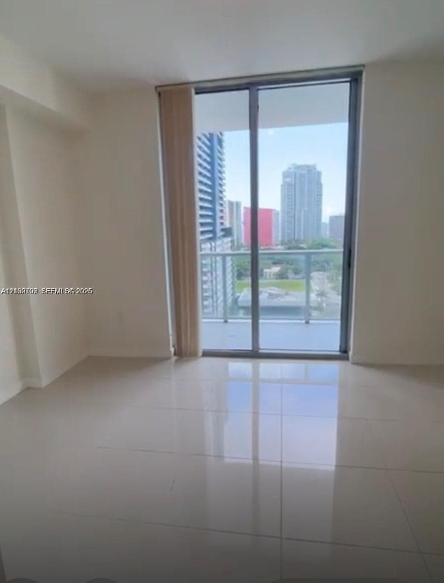 Large-format tile flooring, floor-to-ceiling glass sliding doors, and private balcony featuring a glass railing