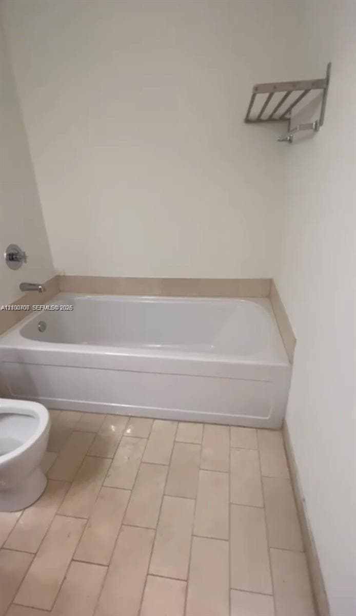 Bathroom featuring a deep soaking tub with a tiled surround, plank-style floor tiling, and a wall-mounted metal towel rack