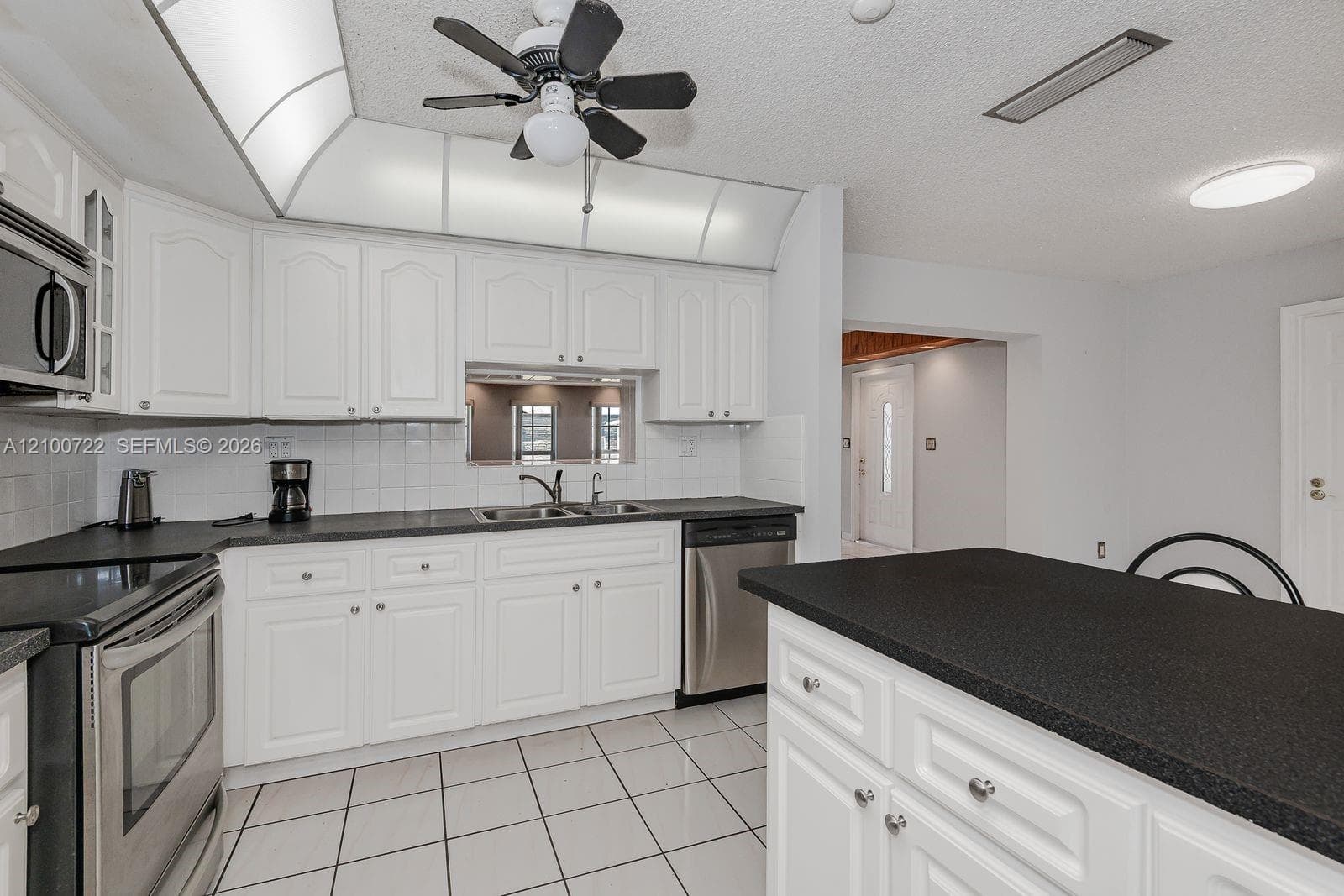 Kitchen featuring white cabinetry, dark solid-surface countertops, tile flooring, stainless steel appliances, and a central island