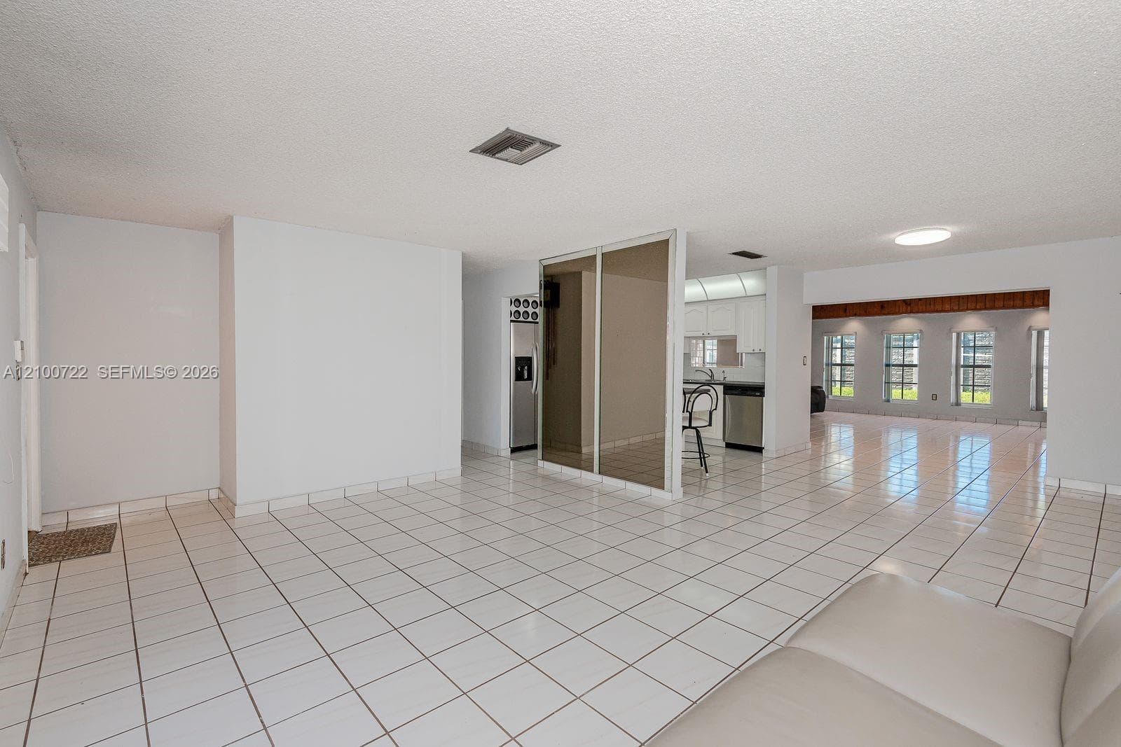 Open interior featuring white ceramic tile flooring, a floor-to-ceiling mirrored partition, and large-format rectangular windows