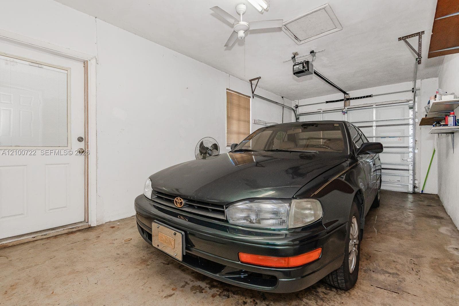 Enclosed garage featuring a metal sectional door, ceiling-mounted paddle fan, concrete flooring, and an exterior-access door with a glass panel
