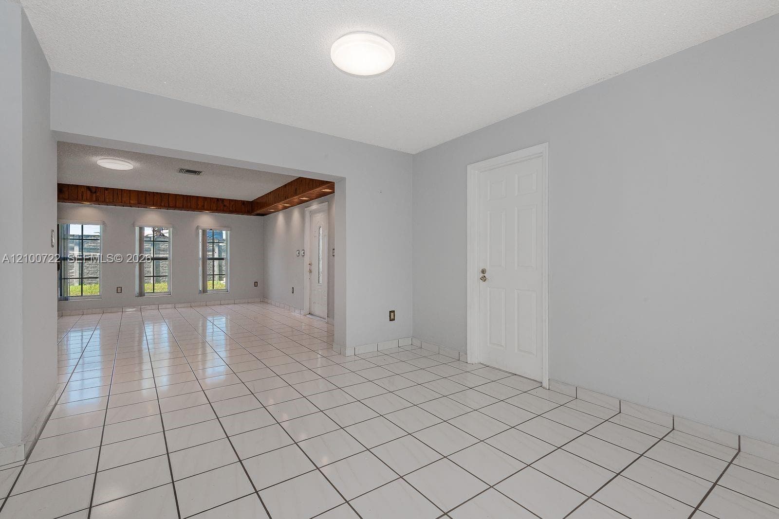 Interior space featuring ceramic tile flooring, neutral wall paint, three large windows, recessed wooden ceiling detailing, and flush-mount ceiling lighting