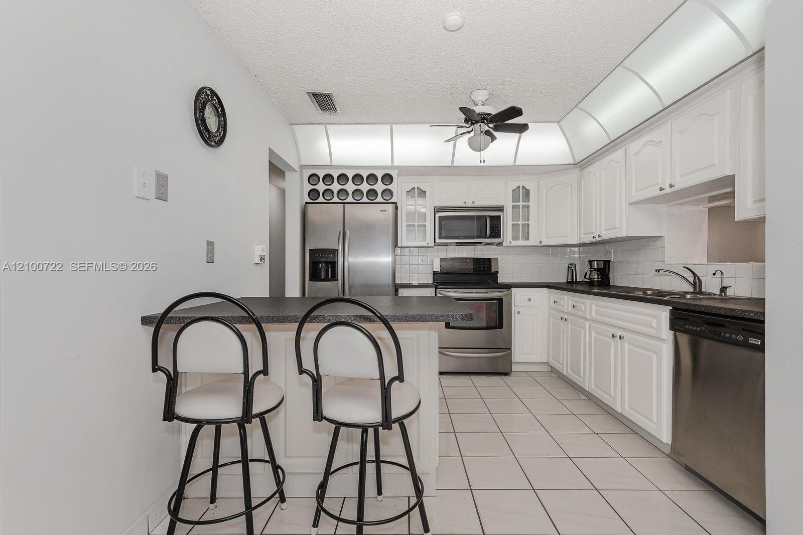 Kitchen featuring white cabinetry, stainless steel appliances, dark countertops, built-in wine rack, and tile flooring