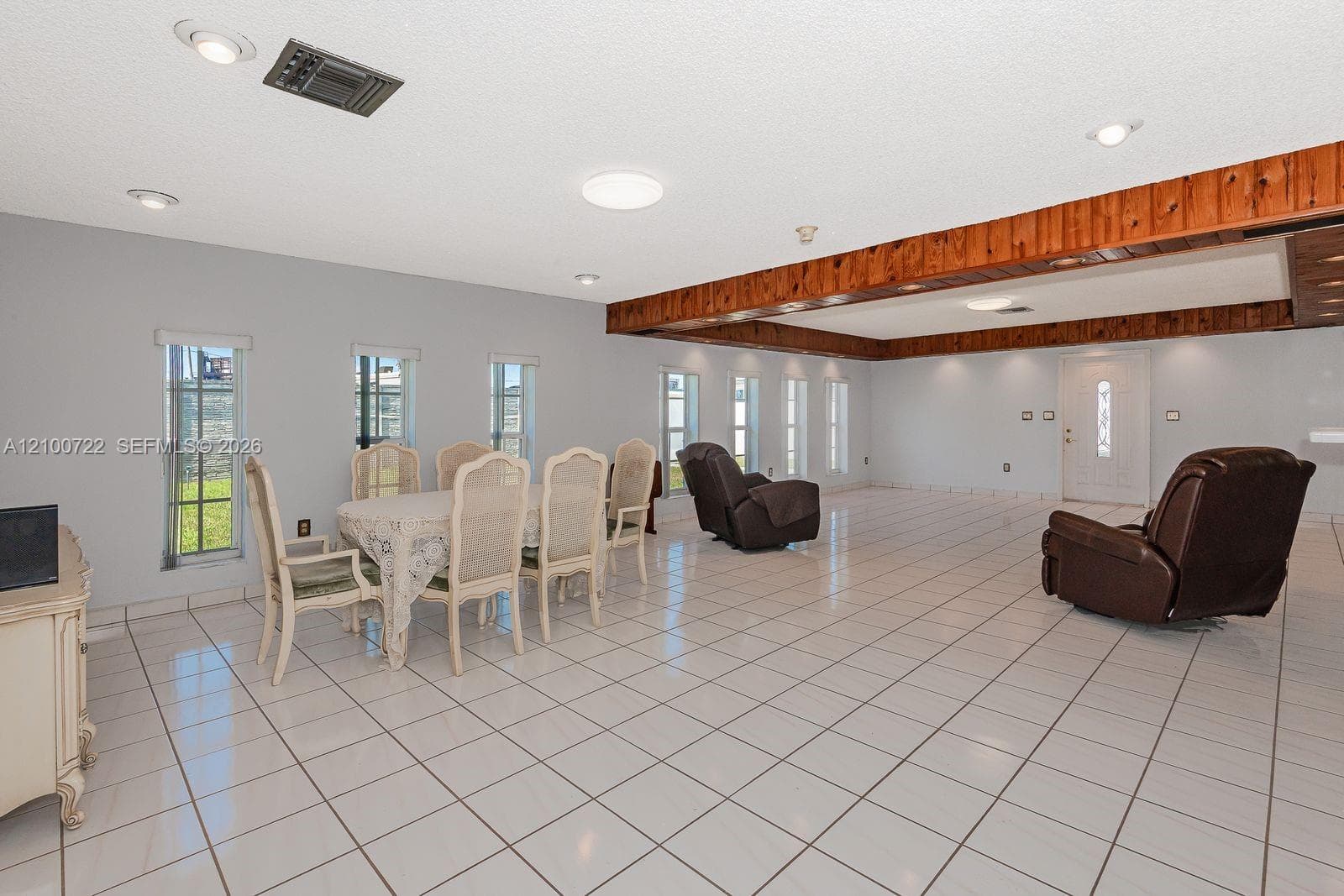 Open-concept room featuring light-toned tile flooring, recessed ceiling lighting, and exposed natural wood ceiling beams