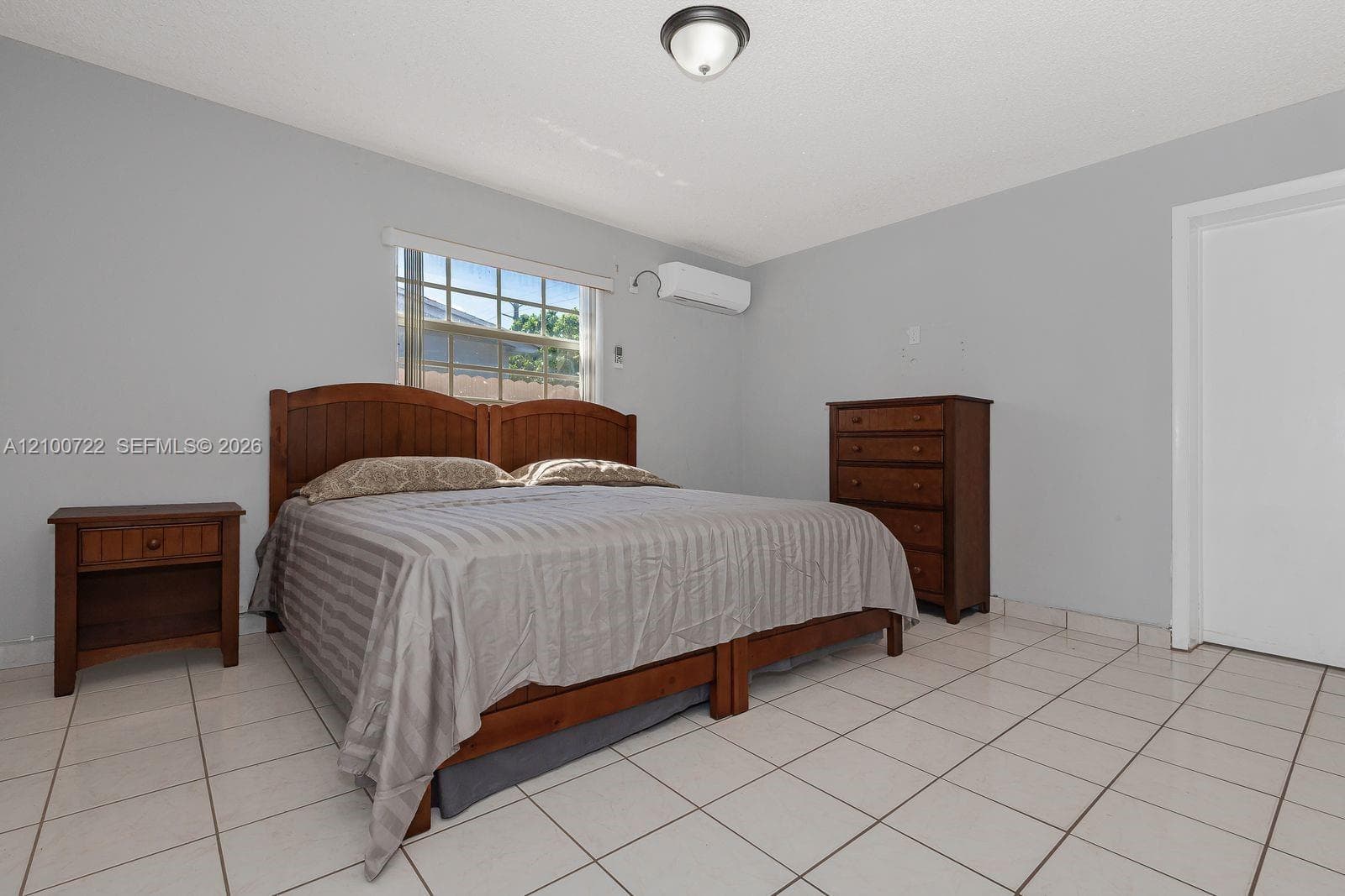 Light-filled room featuring white tile flooring, a multi-pane window, wall-mounted split-system air conditioning unit, and flush-mount ceiling lighting