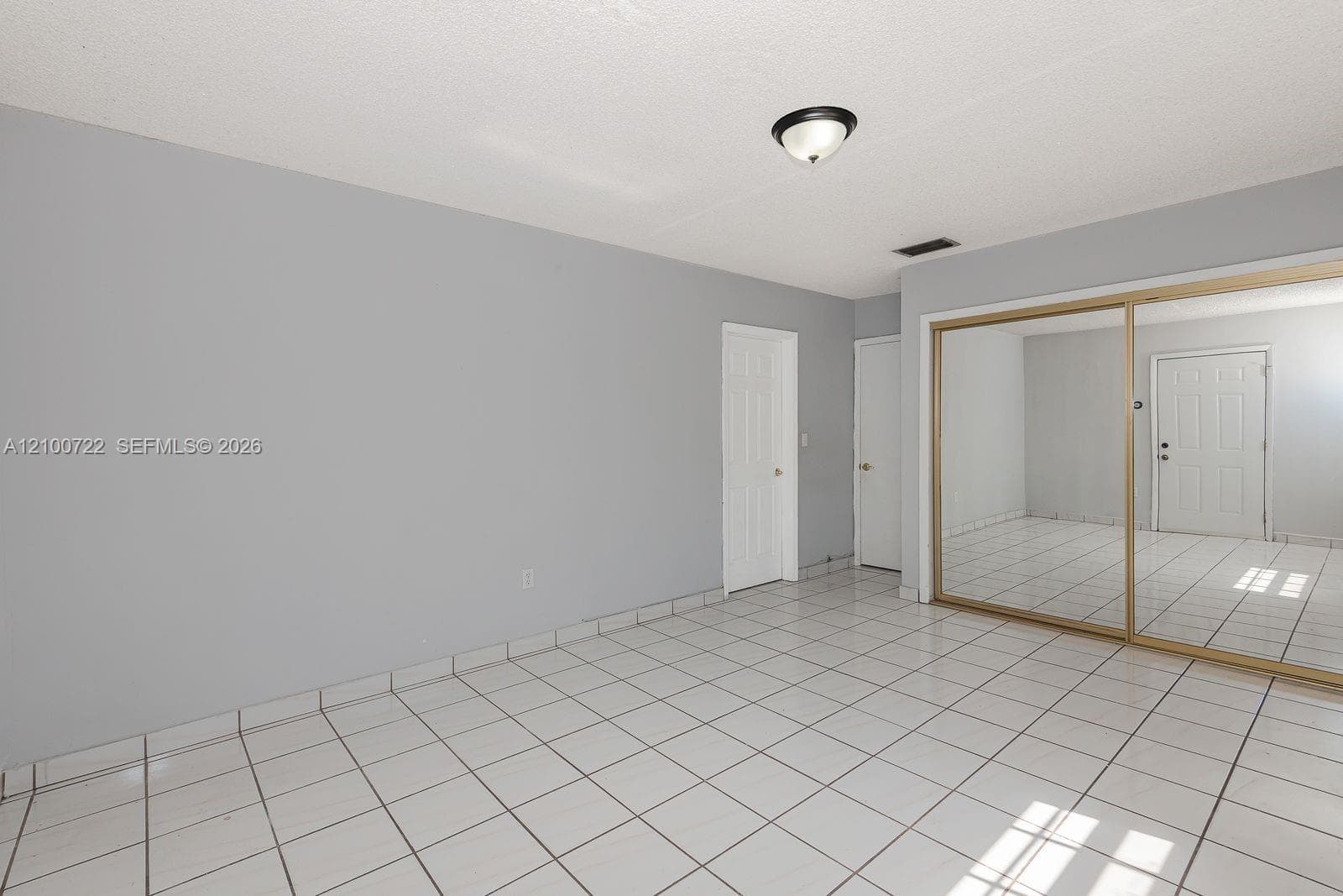 Room featuring white ceramic tile flooring, neutral grey wall paint, two interior doors, and a sliding mirrored closet door