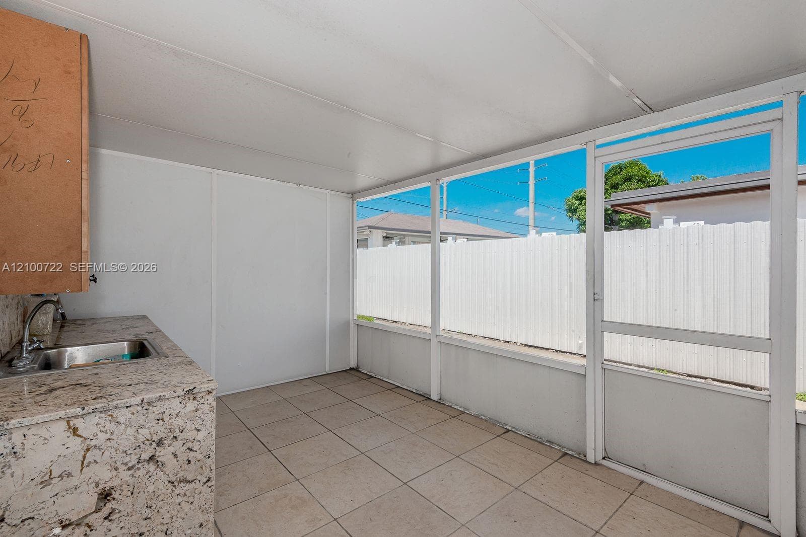Screened-in patio featuring a tile floor, stone-composite countertop, stainless steel sink, and a white privacy fence