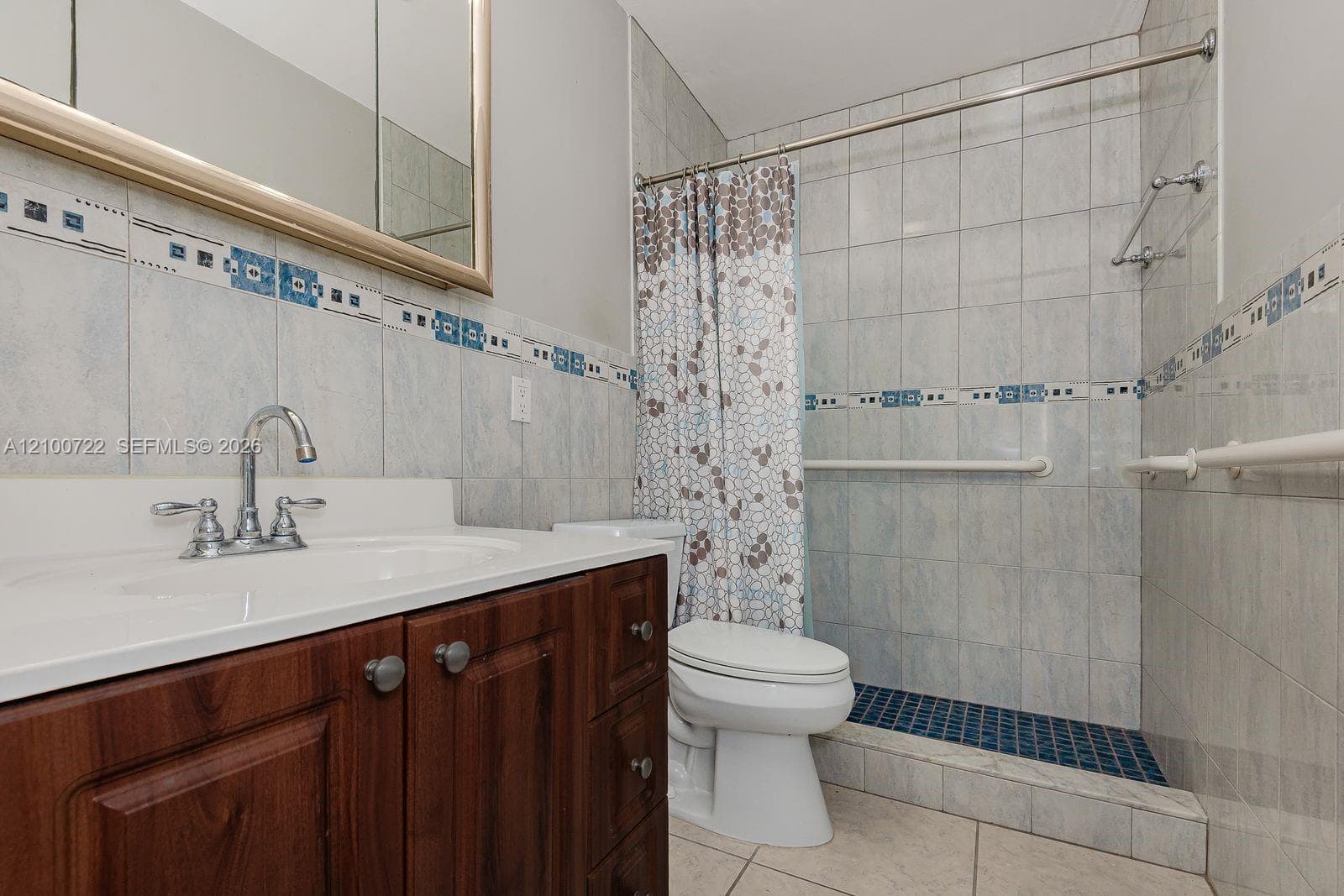 Bathroom featuring a wood-finish vanity with a white countertop, an integrated sink, decorative tile accents, and a walk-in shower with tiled walls and flooring