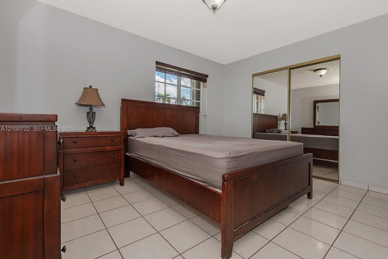 Neutral wall tones, ceramic tile flooring, sliding mirrored closet doors, and a multi-pane window with wood-finish blinds