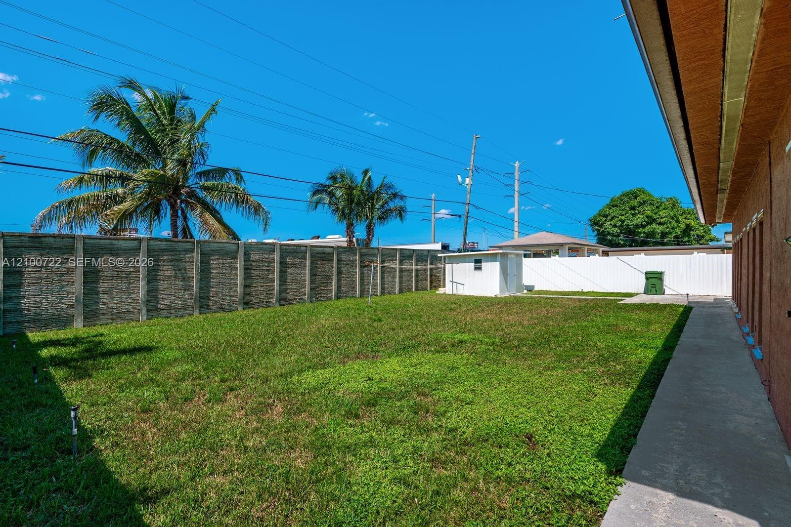 Private backyard featuring a concrete perimeter wall, secondary white vinyl fencing, lawn area, concrete walkway, and a detached storage structure