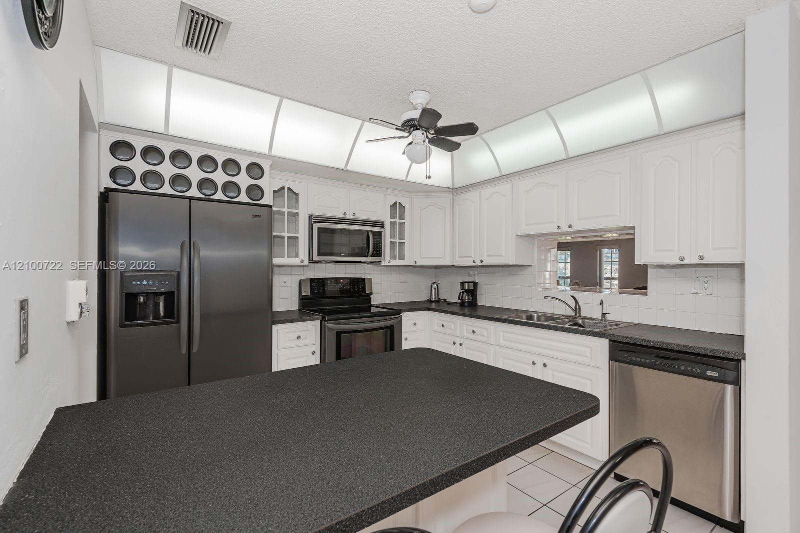 Kitchen featuring white cabinetry, dark solid-surface countertops, integrated stainless steel appliances, a tiled backsplash, and recessed soffit lighting