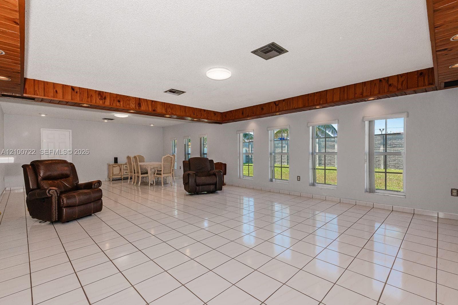 Expansive interior space featuring white tile flooring, natural wood-trimmed ceiling molding, and multiple vertical windows