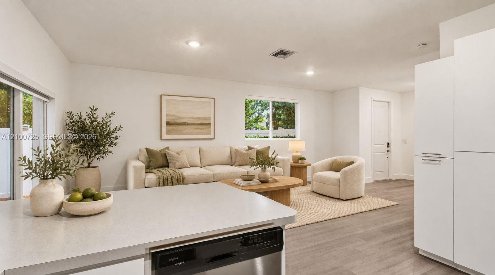 Open-concept living space featuring wood-finish flooring, recessed lighting, matte white cabinetry, stone-finish countertops, and sliding glass doors