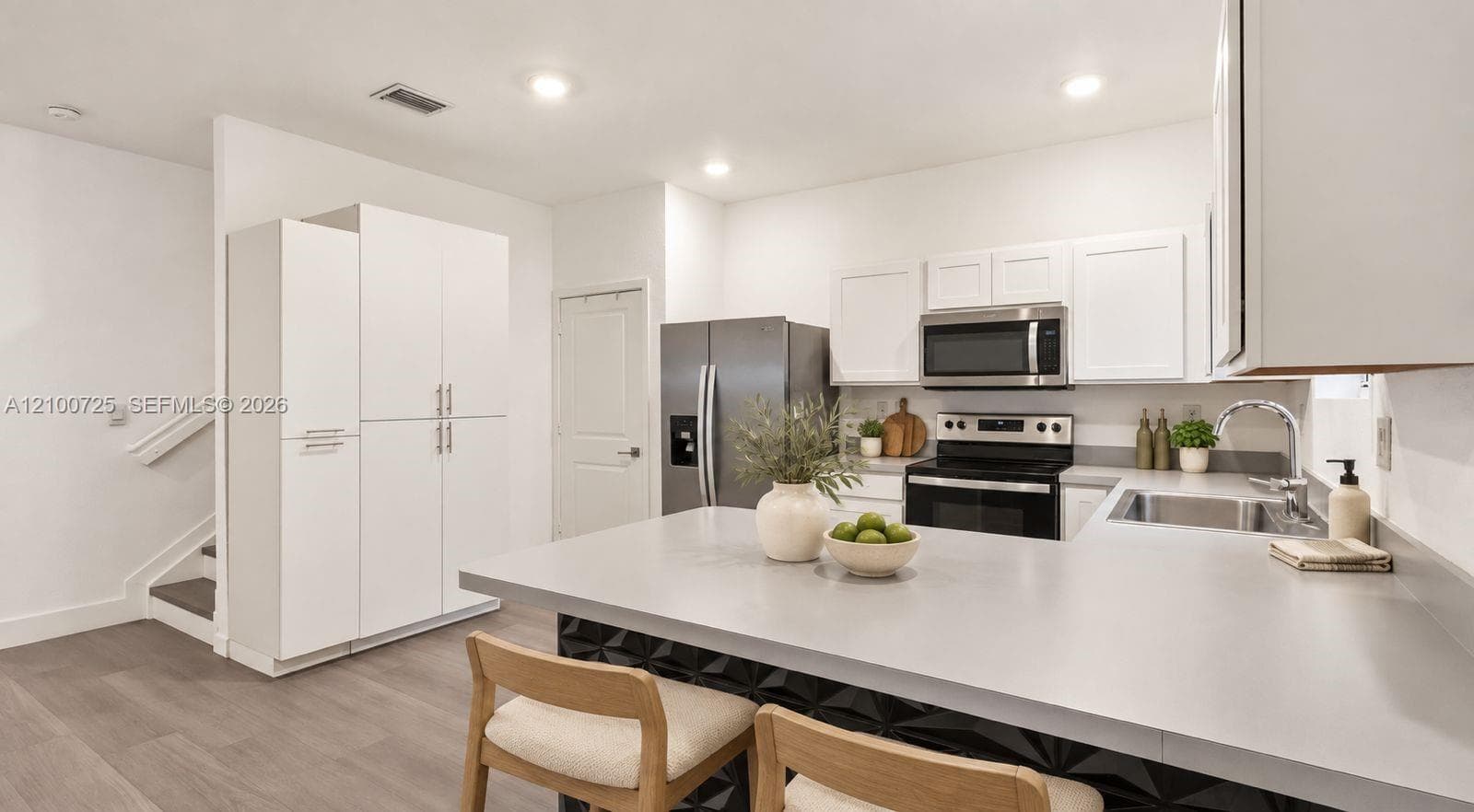 Kitchen featuring white shaker-style cabinetry, an expansive island with a solid-surface countertop, stainless steel appliances, and wood-finish flooring