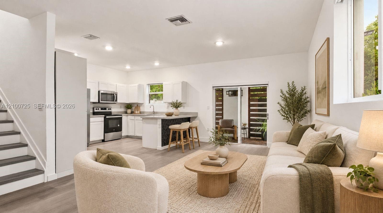 Open-concept living space featuring wood-finish flooring, recessed lighting, white cabinetry, stainless steel appliances, and sliding glass doors