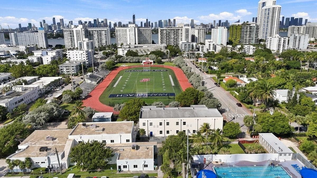 Outdoor recreational complex featuring multiple tennis courts, a practice wall, a swimming pool, and manicured landscaping with mature palm trees
