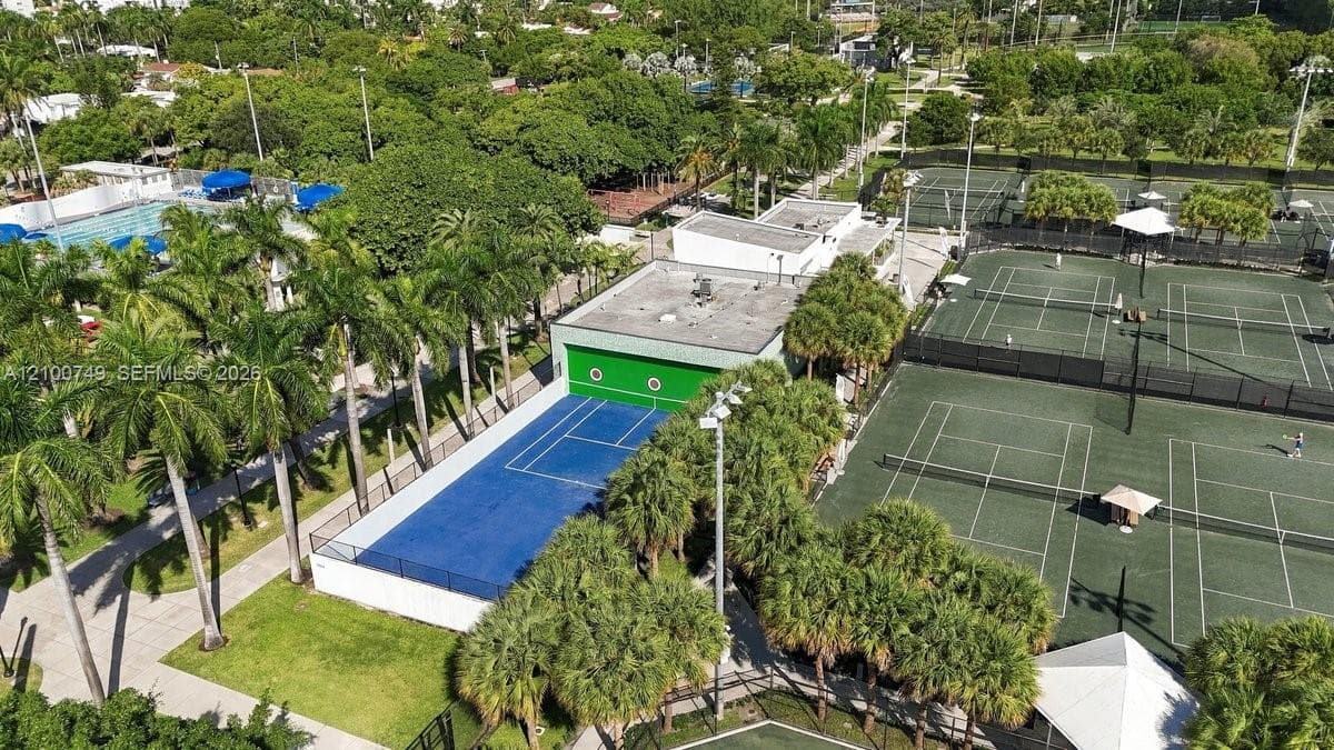 Aerial view featuring dual basketball courts, concrete paved walkways, mature trees, and detached auxiliary structures