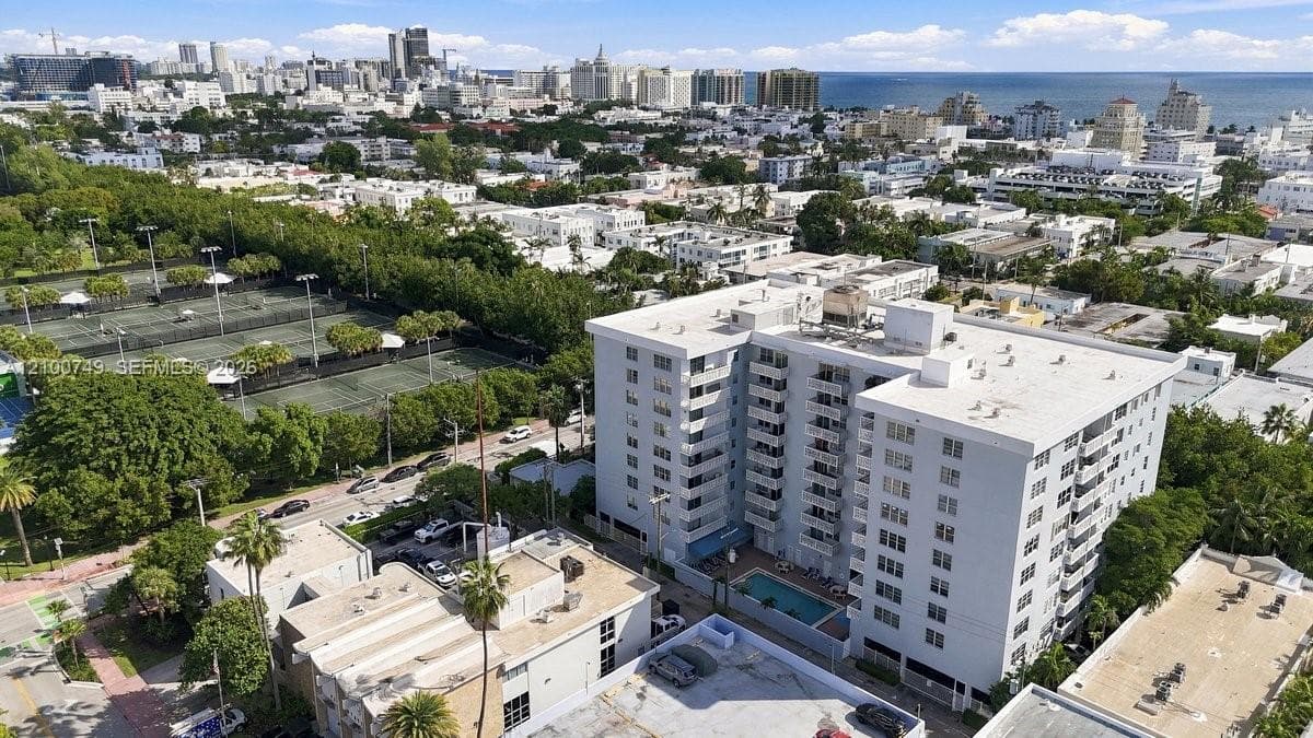 Mid-rise residential building featuring stacked balconies, an in-ground swimming pool, and proximity to public tennis courts within a coastal urban setting