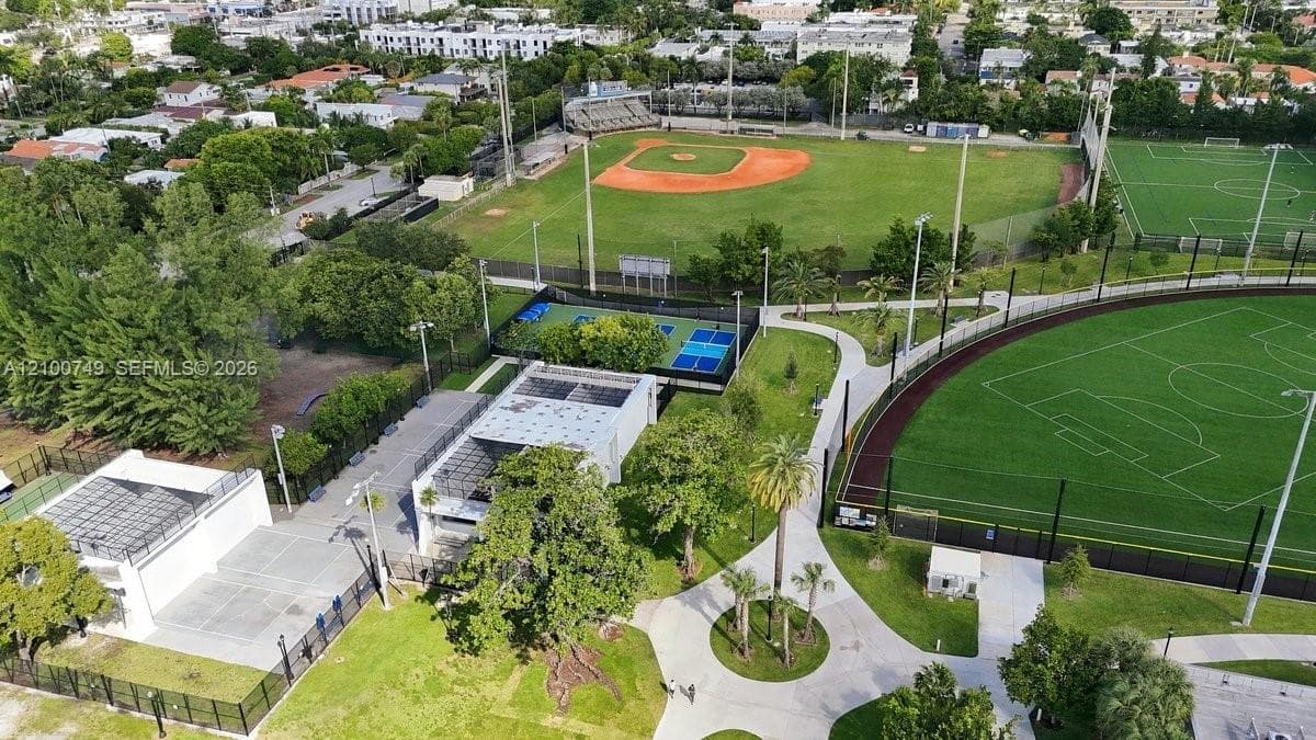 Aerial perspective featuring multi-use athletic courts, baseball fields, paved walking paths, expansive green spaces, and mature landscaping