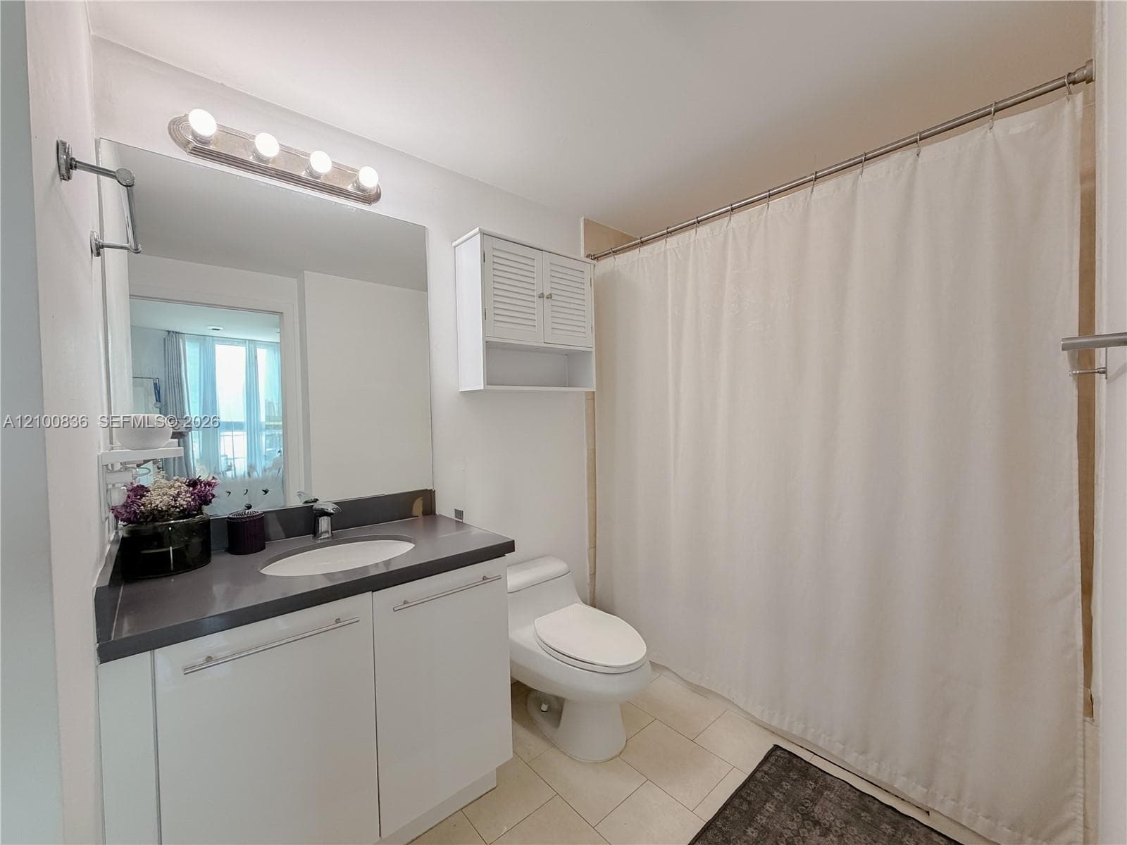 Bathroom featuring a solid-surface countertop with an integrated basin, white cabinetry, a wall-mounted louvered storage cabinet, and a five-light vanity fixture