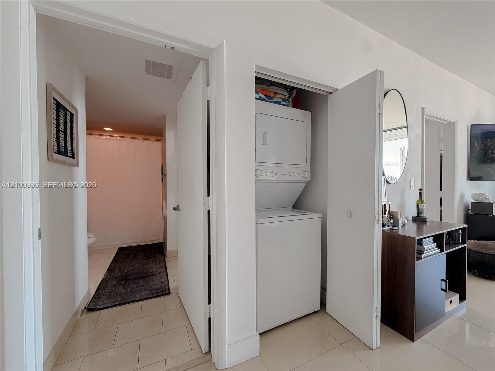 In-unit closet laundry area featuring a stacked washer and dryer, finished with tile flooring