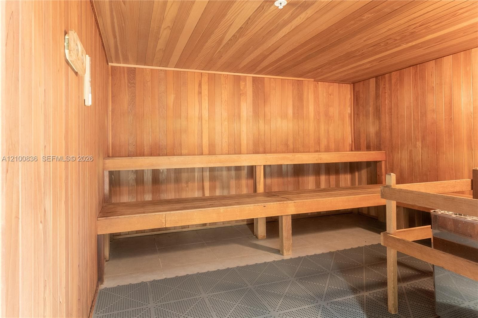 Sauna featuring tongue-and-groove wood paneling, multi-level built-in wood bench seating, and an integrated heating unit with protective guard rail