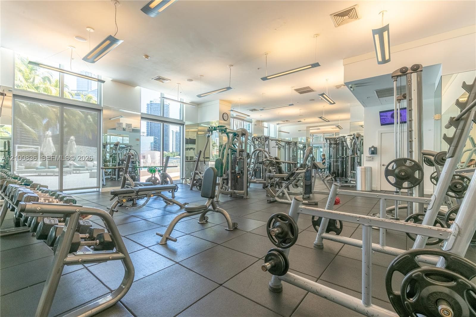 Fitness facility featuring rubberized flooring, linear pendant lighting, floor-to-ceiling windows, and wall-to-wall mirrors