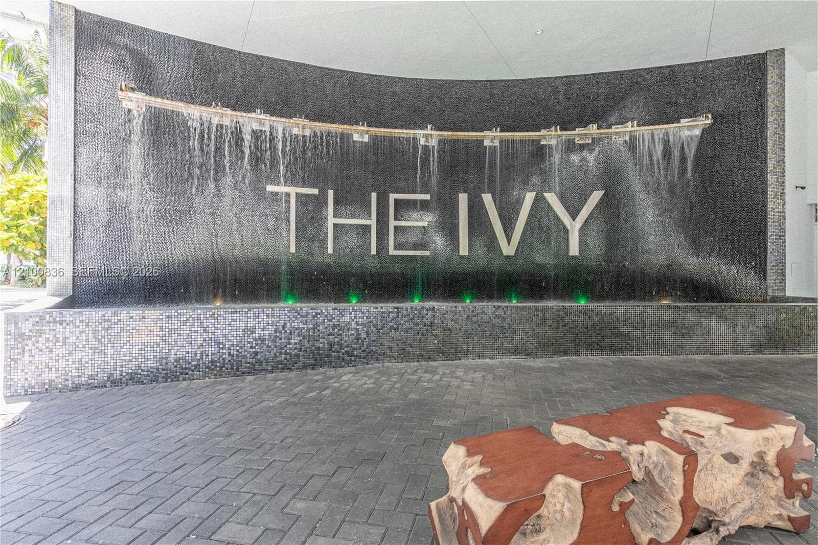 Curved black tile feature wall with integrated waterfall, stone-tiled basin, and dark paver flooring
